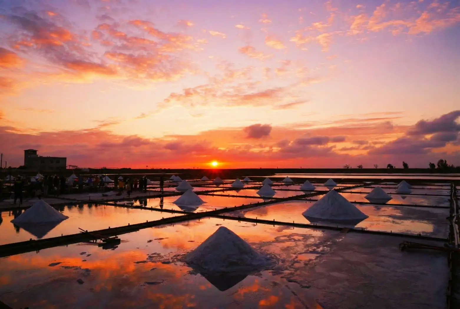 夕陽映照北門井仔腳瓦盤鹽田，金黃天際倒映在鹽田水面，鹽堆與人影交織成靜謐畫面，見證2025年最後一道夕陽的溫柔時刻。(圖/雲嘉南濱海國家風景區管理處提供)