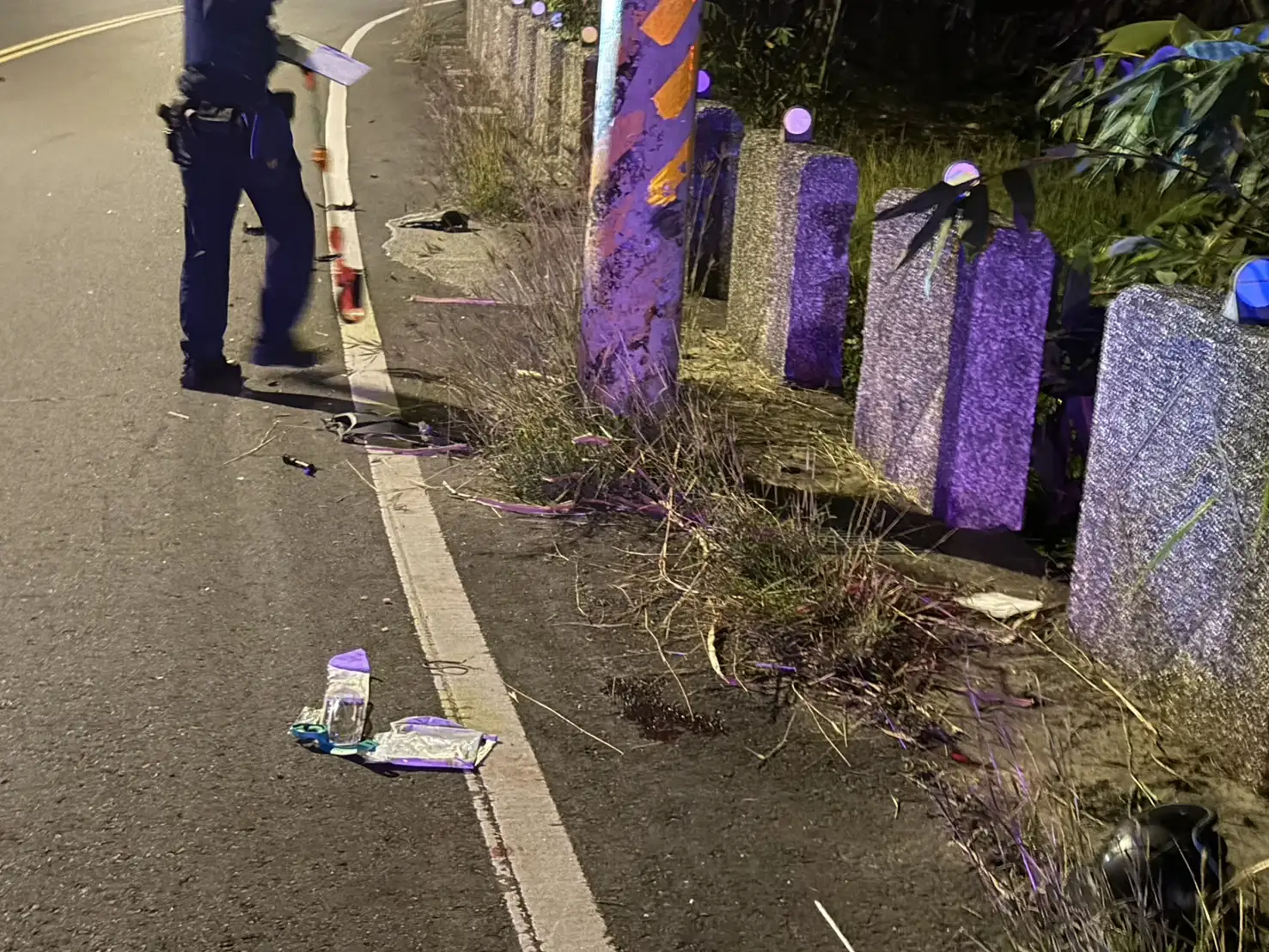 嘉義縣梅山鄉公園西街彎道事故現場電桿與路旁護欄可見明顯撞擊痕跡，車體碎片與物品散落路面，警方到場進行勘查釐清事故原因。(圖/竹崎分局提供)