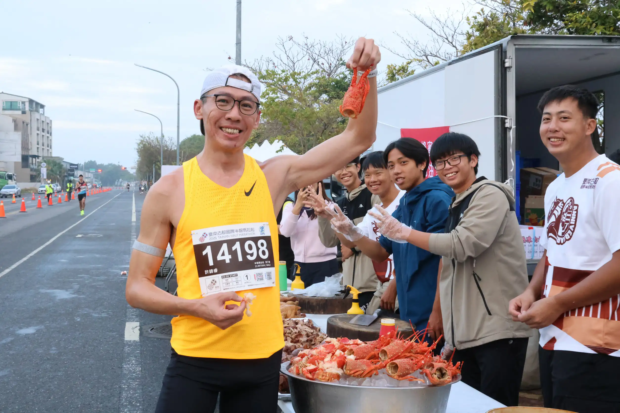 跑者於補給站開心舉起龍蝦享用美食，本屆臺南古都國際半程馬拉松首度結合米其林餐廳與在地特色料理，升級補給內容，成為賽事亮點之一。(圖/台南市政府提供)