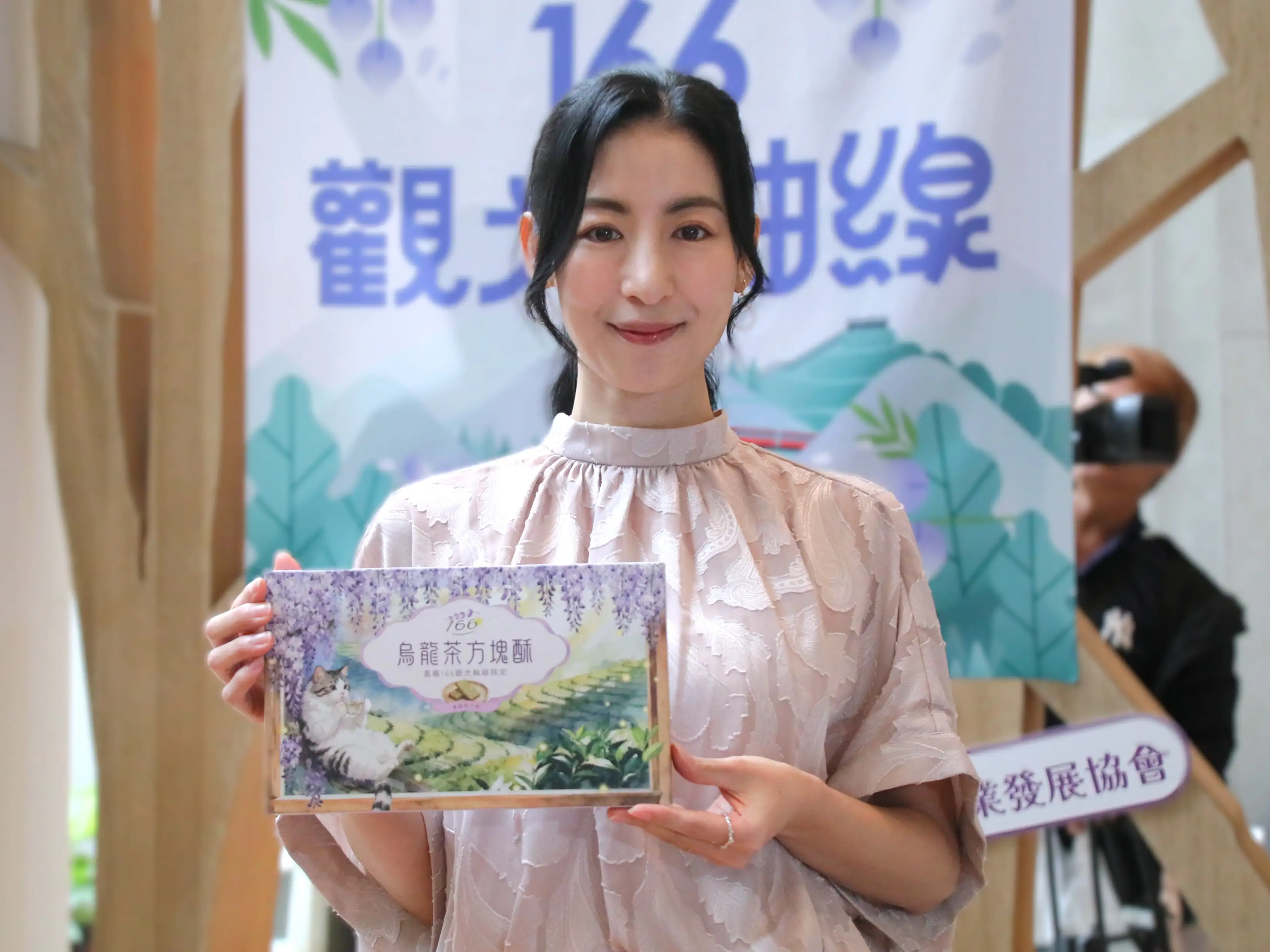 藝人大久保麻梨子出席「2026瑞里紫藤花季」宣傳記者會，手持瑞里特色商品，推薦民眾到嘉義瑞里賞花、品茶與體驗山城慢遊。（圖/嘉義縣文化觀光局提供）
