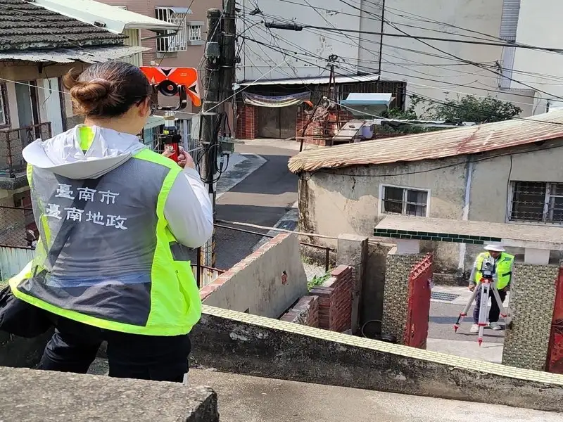 台南市地政人員於北區進行地籍圖重測作業，一人於高處操作測量儀器進行定位，另一人於巷內架設設備同步量測，透過前後對位精準確認土地界址，呈現實地重測作業的專業流程。（圖／臺南市政府地政局提供）