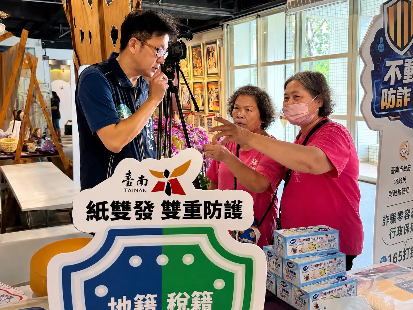 地政局人員於活動會場向市民解說「地籍異動即時通」及「稅籍異動即時通」服務內容，鼓勵民眾善用即時通知機制，及早掌握不動產異動資訊，共同防範房地產詐騙案件發生。(圖/台南市地政局提供)
