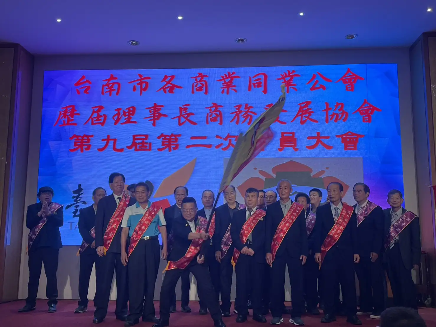 台南市各商業同業公會歷屆理事長商務發展協會第九屆第二次會員大會暨25週年慶典中，理事長楊富翔揮舞會旗，象徵薪火相傳、團結凝聚會員向心力，帶領協會邁向嶄新里程碑。(記者林怡孜攝)
