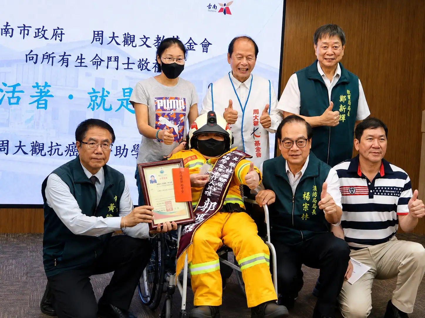 懷抱消防夢的抗癌學子穿上消防衣體驗，現場貴賓共同為他加油打氣，鼓勵勇敢逐夢。（圖/臺南市政府提供）
