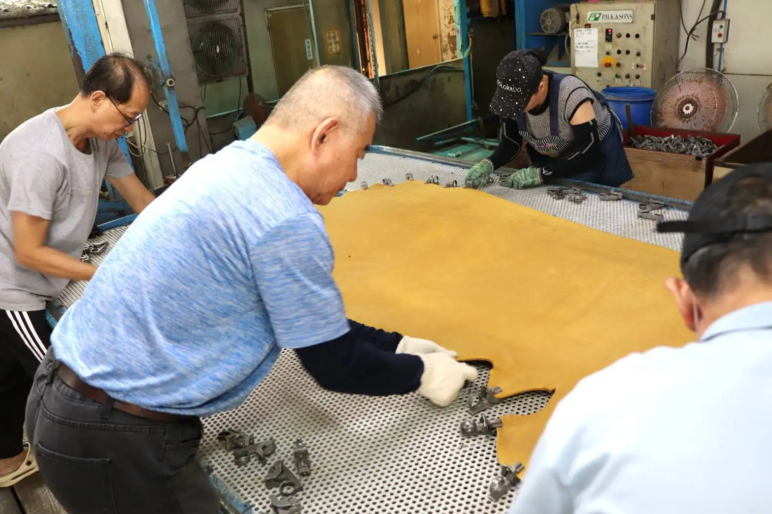 阿三(中)與同事通力合作一起拔除固定皮革拉伸及乾燥的特製夾子，已逐漸熟練。