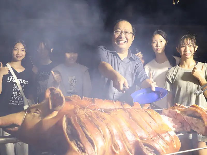 中華醫大新生訓練之夜舉辦迎新烤肉，校長孫逸民開心與新生分享烤全豬。(圖/中華醫事科技大學 提供)