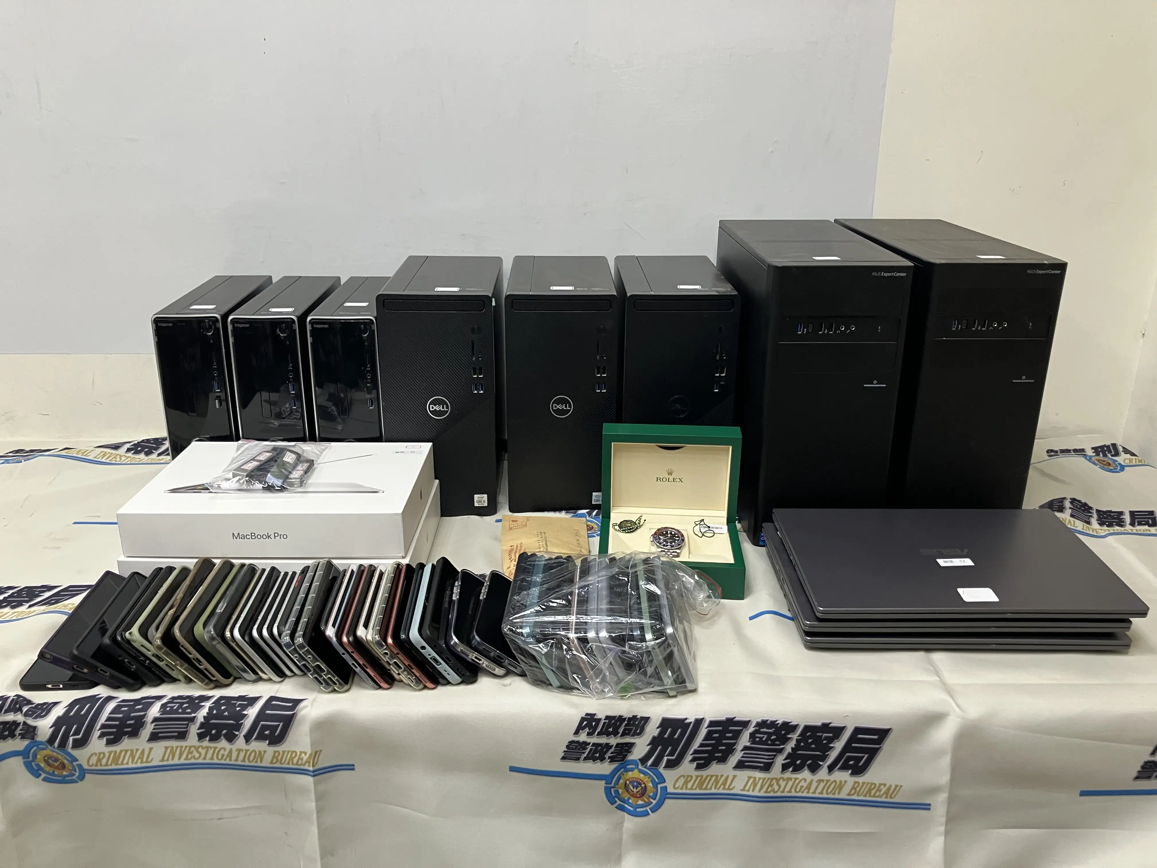 警方破獲跨境洗錢機房,現場查扣多部主機、筆記型電腦、手機、MacBook Pro、名錶、現金及作業工具等贓證物。(圖/刑事局電偵大隊提供)