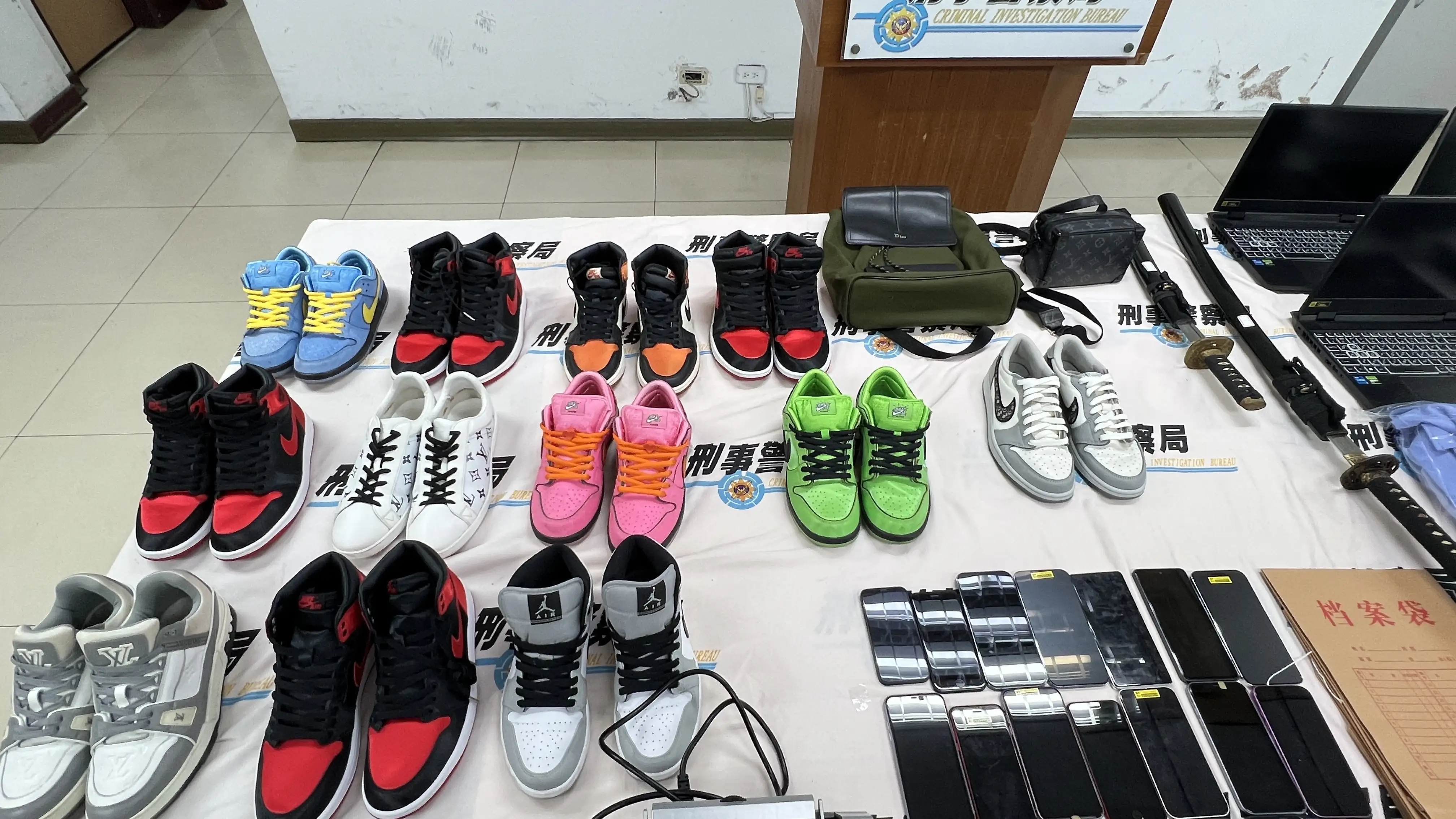 警方查扣跨境詐團假公安制服及臂章、名牌包、名牌鞋、手機、筆電與桌機、現金23萬2600元、監視器設備、毒品K他命與吸食盤、武士刀等大量贓證物。(圖/刑事局提供)