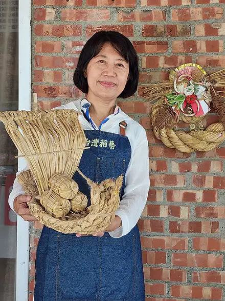 「台灣稻藝」負責人張淑娥與稻草手編寶船。牆壁上懸掛著日本石川縣指定型式的注連繩。(圖/臺南市政府觀光旅遊局 提供)