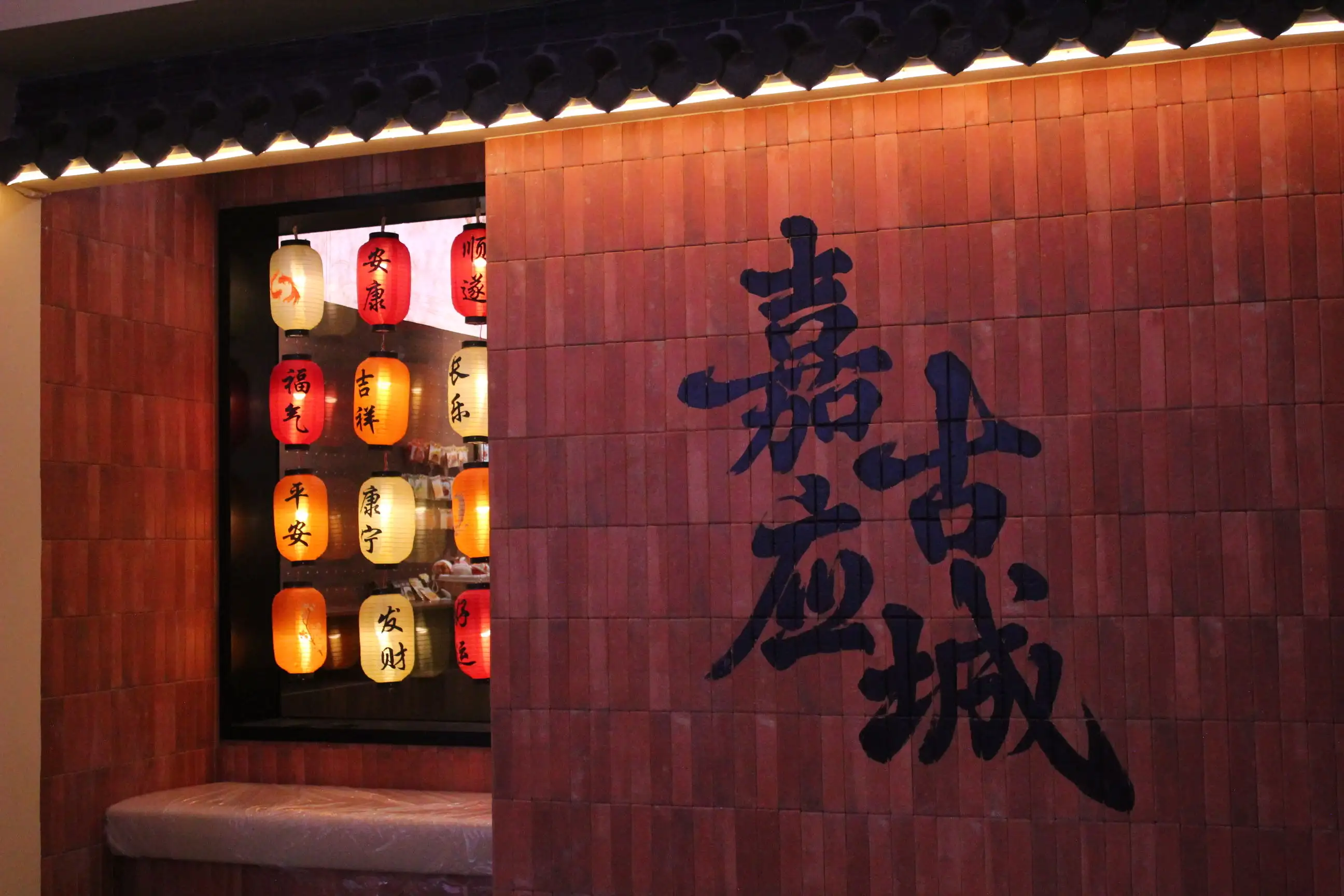 溫暖燈影映照下的嘉應古城字樣外牆，窗內掛飾的彩色燈籠訴說著祝福與人情味，展現古城濃厚的文化氛圍與夜色魅力。(楊婉提供)